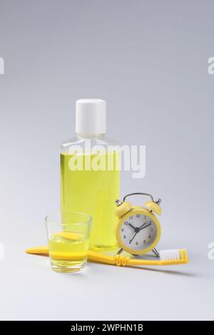 Fresh mouthwash in bottle, glass, toothbrush and alarm clock on grey background Stock Photo