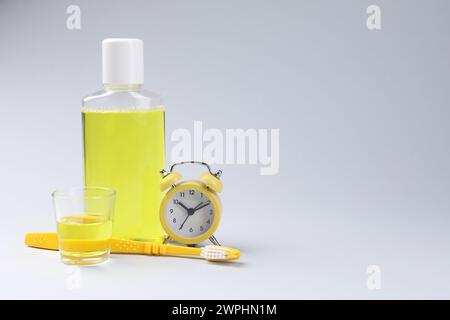 Fresh mouthwash in bottle, glass, toothbrush and alarm clock on grey background. Space for text Stock Photo
