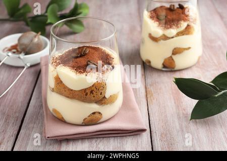 Delicious tiramisu with coffee beans in glasses and green leaves on wooden table Stock Photo