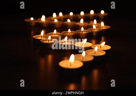 Burning candles on surface in darkness, closeup Stock Photo