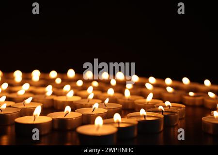 Burning candles on dark surface against black background Stock Photo