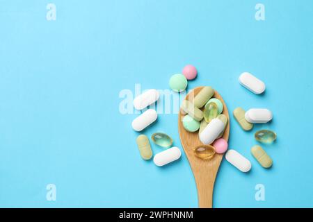 Different vitamin pills in wooden spoon on light blue background, top view. Space for text Stock Photo