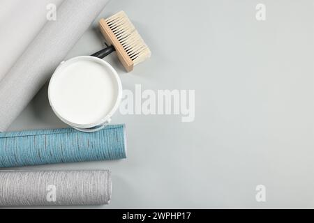 Different wallpaper rolls, brush and bucket with glue on light background, flat lay. Space for text Stock Photo