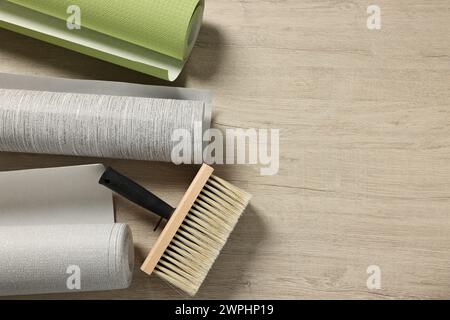 Different wallpaper rolls and brush on wooden table, flat lay. Space for text Stock Photo