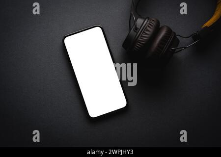 Retro style wireless over-ear headphones and smartphone with blank screen on dark gray background Stock Photo