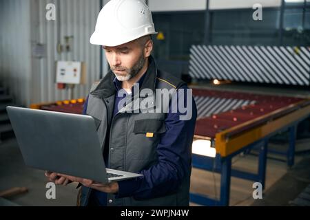 Man with a laptop stands in a production workshop Stock Photo