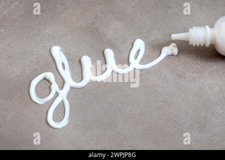 The word glue written with white wood glue on a mottled grey surface with copy space Stock Photo