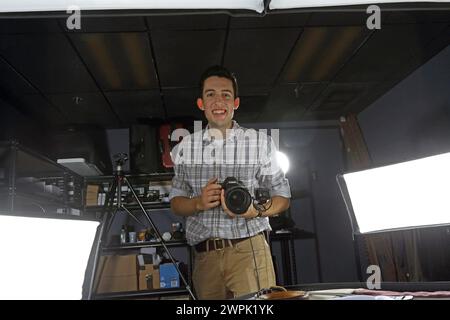 Professional photographer posing in the studio and holding a digital camera, he is ready for the photo shoot. Stock Photo