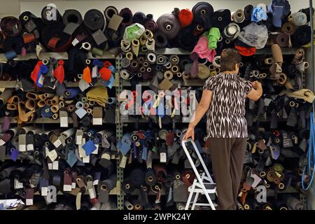 female choosing from rolls of fabric in textiles factory . Stock Photo