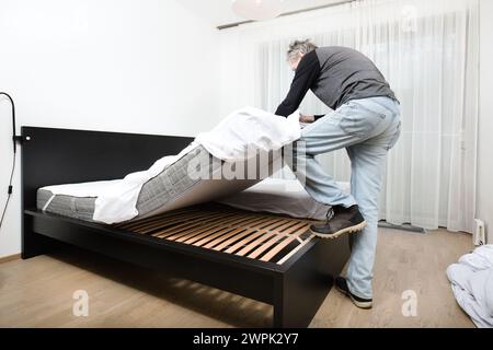 Older man working in bedroom on making bed Stock Photo