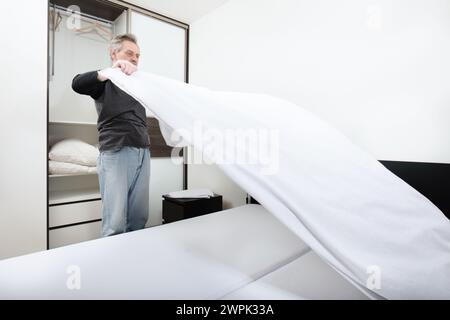 Older man working in bedroom on making bed Stock Photo