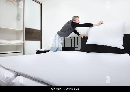 Older man working in bedroom on making bed Stock Photo