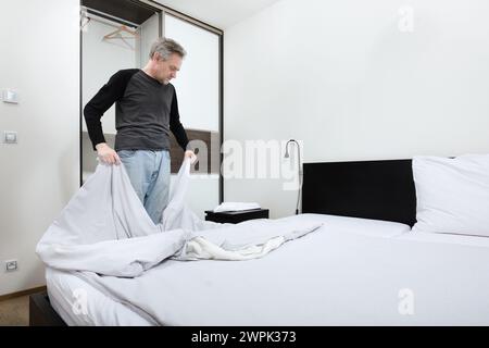 Older man working in bedroom on making bed Stock Photo