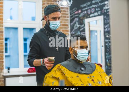 Indian client and barber wearing a mask in a barbershop - Getting hair trimmed. High quality photo Stock Photo