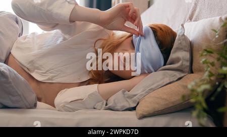 Sleeping napping lazy Caucasian girl with blindfold in bed in early morning peek out from under sleep mask open eye fall asleep again woman sleepy Stock Photo