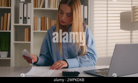 Caucasian woman girl businesswoman using calculator and laptop app calculate costs incomes money doing office paperwork check expenses business Stock Photo