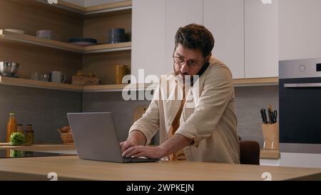 Caucasian multitasking man with laptop working from home talking mobile phone business freelancer businessman at quarantine. Male client order food Stock Photo
