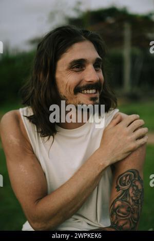 Portrait of smiling young man with long brown hair and dark eyes. Stock Photo