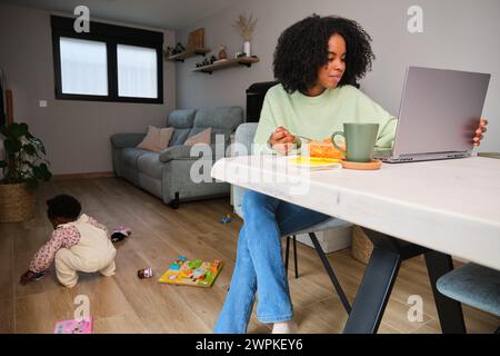 Cuban mother eating, working a taking care of her toddler daughter. Stock Photo