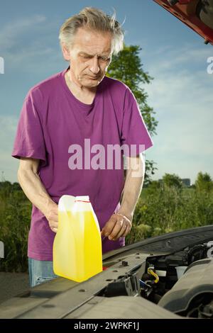 Older driver on longer trip topping up tank with washer fluid Stock Photo