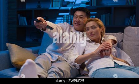 Multiracial couple watch movie at night evening diverse married Asian man and Caucasian woman happy family multiethnic Korean husband and wife Stock Photo