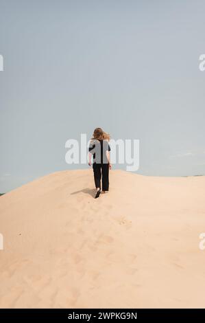 Back view of woman hiking up sand dunes with hair flowing in the wind Stock Photo