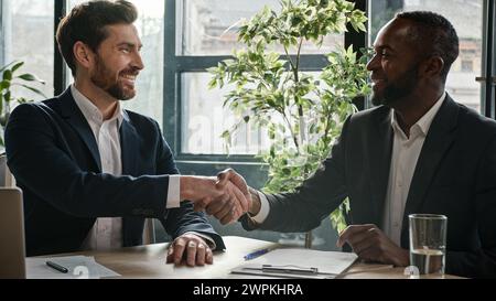 Two diverse multiracial businessmen signing document agreement shaking hands success business deal. Multiethnic men partners in office meeting Stock Photo
