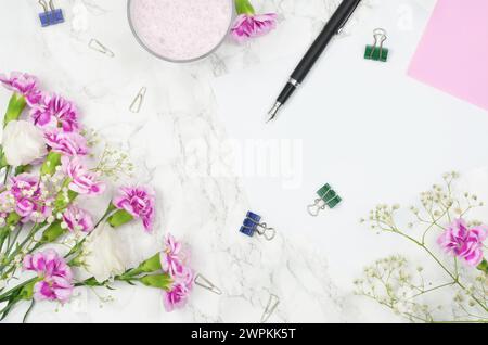 Pastel colors, flowers, blank sheet of paper to fill in, pen on a table, top view. Stock Photo