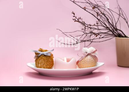 Eggs decorated artisanal nets and ribbons on white plate. Branch and candles simple pastel rustic background for traditional Easter holiday card Stock Photo