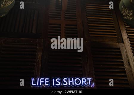 The neon sign on the wall says LIVE IS SHORT. Stock Photo