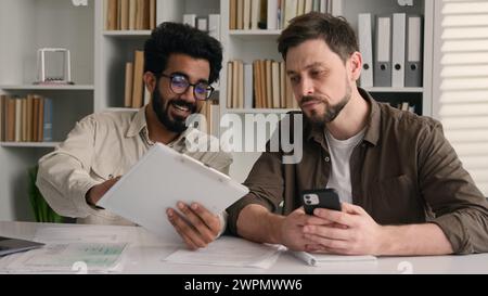 Two businessmen multiracial men co-workers in office Arabian Indian businessman show papers business project on laptop to colleague Caucasian man Stock Photo