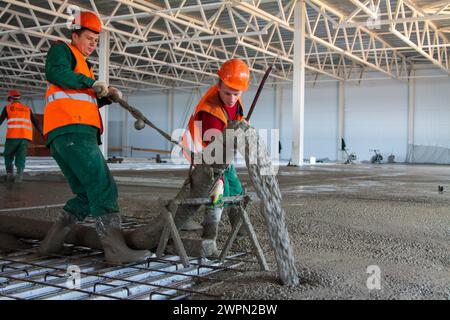 two Caucasian workers pouring concrete floor in large industrial hangar building Stock Photo