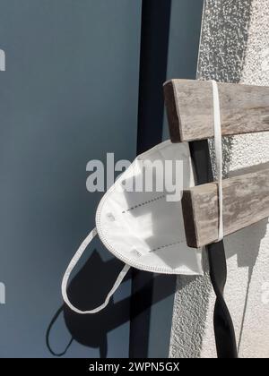 White FFP2 mask hangs outside on the back of a chair in the sunlight Stock Photo