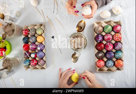 human hands of two sorbian women are painting with melting wax with a trimmed goose quill and a needle head on the surface of the egg at a Table with Stock Photo