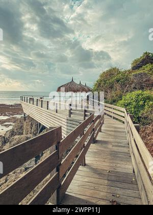 Wooden deck with straw beach umbrellas and sunset view in Uluwatu cliff, Bukit Peninsula, Bali. Stock Photo