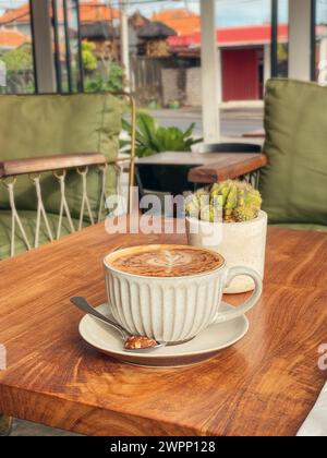 A cup of coffee with latte art on top on wooden table in cafe closeup Stock Photo