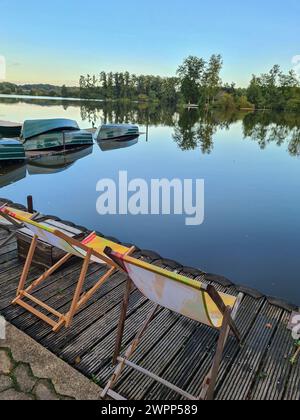 Two deckchairs on a wooden jetty on the shore with a view of boats, blue sky on the horizon and in the water reflection, Germany Stock Photo