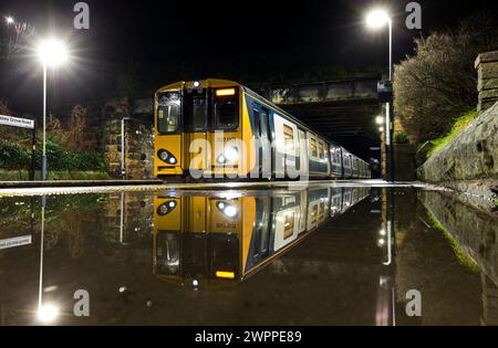 Merseyrail class 507 electric train 507001 calling at Wallasey Grove Road Railway station, on the Wirral line, reflected in a puddle on the platform Stock Photo