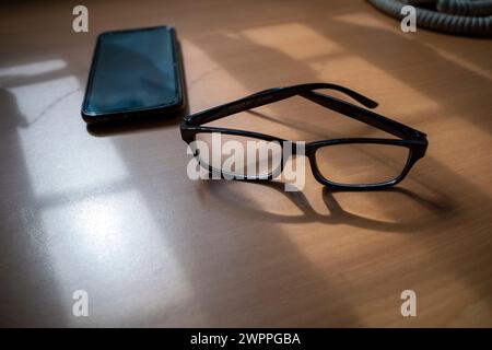 A business desk table with eyeglass and a smartphone. Wood background with copy space. Stock Photo