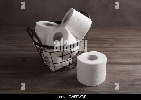 Soft toilet paper rolls in metal basket on wooden table Stock Photo