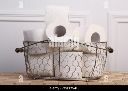 Soft toilet paper rolls in metal basket on wicker table, closeup Stock Photo