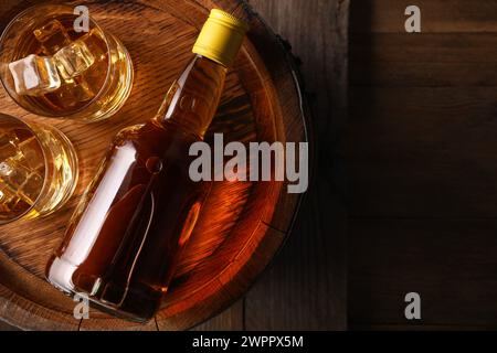 Whiskey with ice cubes in glasses, bottle and barrel on wooden table, top view. Space for text Stock Photo