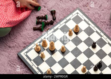 Young child playing chess pieces laid out on the ground, soft purple carpet the chessboard reveals an in-progress game Clever intelligent kids playing Stock Photo