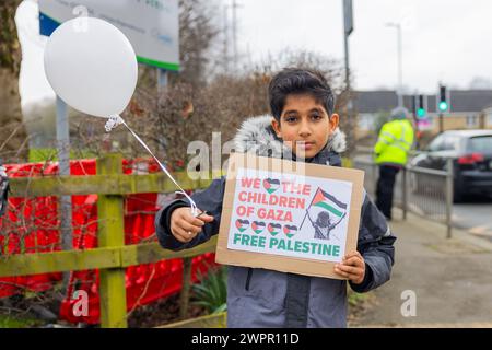 Bingley, UK. 08 MAR, 2024. Young boy waves balloon while holding Pro Palestine sign. Story: Parents of students at Cottingley Village Primary School pulled their children out at 2PM on the 8th of march as part of a co-ordinated strike effort across multiple different schools across Yorkshire for Palestine. Credit Milo Chandler/Alamy Live News Stock Photo