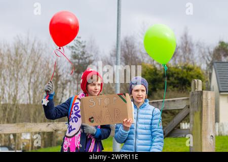 Bingley, UK. 08 MAR, 2024. Two young girls hold different colour balloons and hold 'Stop the war' sign outside Cottingley primary school. Story: Parents of students at Cottingley Village Primary School pulled their children out at 2PM on the 8th of march as part of a co-ordinated strike effort across multiple different schools across Yorkshire for Palestine. Credit Milo Chandler/Alamy Live News Stock Photo