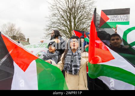 Bingley, UK. 08 MAR, 2024. Young girl waves two Palestine flags alongside fellow pupils at the Cottingley village primary school. Story: Parents of students at Cottingley Village Primary School pulled their children out at 2PM on the 8th of march as part of a co-ordinated strike effort across multiple different schools across Yorkshire for Palestine. Credit Milo Chandler/Alamy Live News Stock Photo