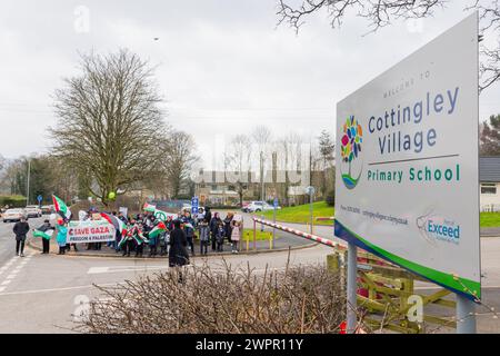 Bingley, UK. 08 MAR, 2024. Gathered protestors stand outside the gates of Cottingley Village Primary school. This picture includes the school's sign. Story: Parents of students at Cottingley Village Primary School pulled their children out at 2PM on the 8th of march as part of a co-ordinated strike effort across multiple different schools across Yorkshire for Palestine. Credit Milo Chandler/Alamy Live News Stock Photo