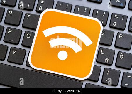 A vibrant orange label badge displaying the universal general Wi-Fi signal strength symbol atop a black desktop PC computer keyboard, wireless network Stock Photo