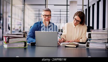 Two Businesspeople Calculating Invoice In Office While Using Laptop Stock Photo
