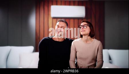 Happy Family Couple Using Air Conditioner. Apartment AC Stock Photo